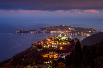Illuminated village of Eze and the Mediterranean Sea at dusk and Saint-Jean-Cap-Ferrat. Alpes-Maritimes, Cote d'Azur, French Riviera, France