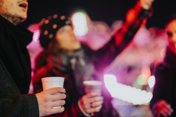 Group of friends sharing joy and laughter while holding warm drinks on a colorful evening. Holiday...