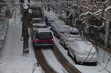 Moment of a storm with strong wind and heavy snowfall on a narrow street with parked cars and a...