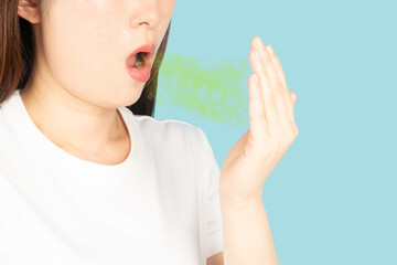 Woman checking her breath oral with hand on blue background. Causes of bad breath (halitosis)...