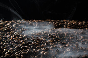Obraz premium Freshly roasted coffee beans with smoke on black background