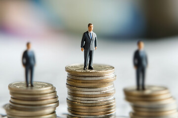 Miniature business figures standing on stacks of coins, symbolizing financial growth, success, and career advancement. Wealth, investment and corporate hierarchy concept. Sharp focus, clean background
