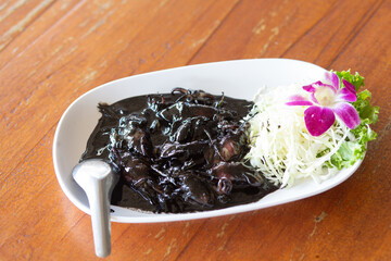Squid stir-fried in black sauce with vegetables on a white plate on a wooden background