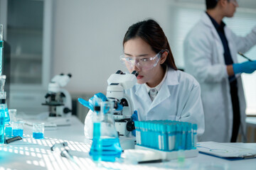 Fototapeta premium Female scientist examining microscope slide with blue liquid solution, research colleague working behind in sterile laboratory setting during medical investigation