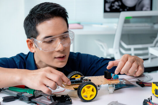 Asian male engineer wearing safety glasses, assembling a robotics toy car in a laboratory setting, utilizing various tools and components to enhance innovation and development in technology