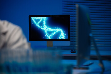 Glowing blue-lit monitor showing rotating DNA double helix animation in dark research laboratory, representing genetic science innovation