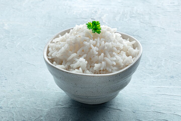 White rice, cooked. A bowl of boiled long grain rice, a simple side dish, with fresh parsley leaves