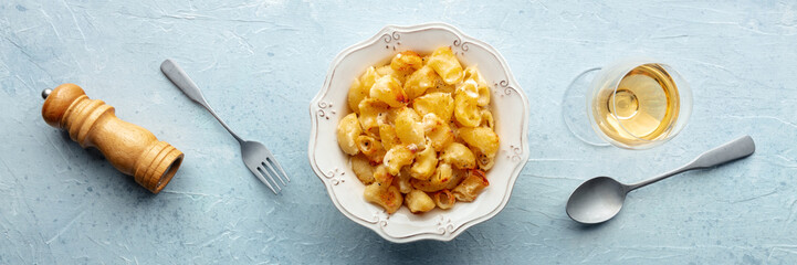 Mac and cheese, the classic pasta with macaroni and Cheddar cheese, baked in the oven, overhead flat lay panorama with a glass of white wine