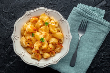 Mac and cheese, the classic pasta with macaroni and Cheddar cheese, with fresh parsley, overhead flat lay shot on a black slate background
