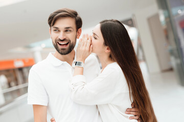 Man and woman in shopping mall. Girl is whispering in man's ear.