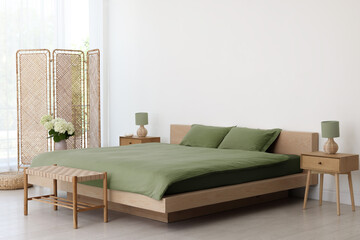Folding screen, comfortable bed, ottoman and bedside tables in room. Interior design