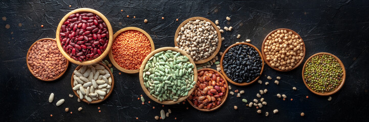 Various legumes, overhead flat lay panorama on a black background. Many different pulses, an assortment, panoramic banner