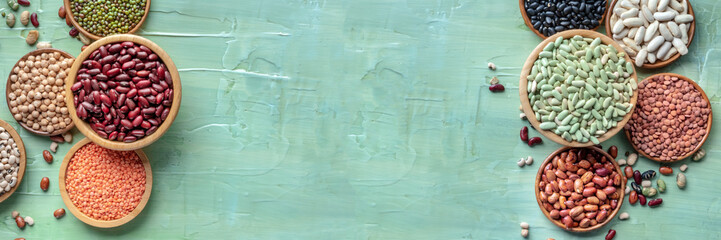 Legumes background panorama. Pulses panoramic banner design with copy space. Many different beans and grains, overhead flat lay shot on blue