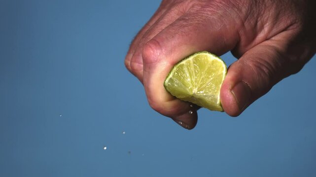 Squeezing the juice from a fresh lime segment,  blue BG super slowmo 2000fps