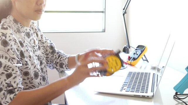 A woman is working on a project on a desk. She is holding a yellow object and is surrounded by tools
