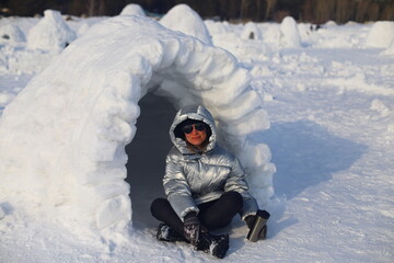 Adult happy woman relaxing on picnic in Eskimo village. Woman in warm down jacket near Igloo.
