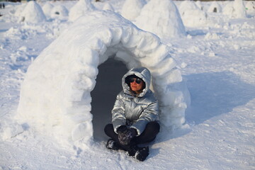 Adult happy woman relaxing on picnic in Eskimo village. Woman in warm down jacket near Igloo.