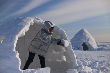 A happy adult woman builds an Igloo out of snow blocks in the Eskimo Village.