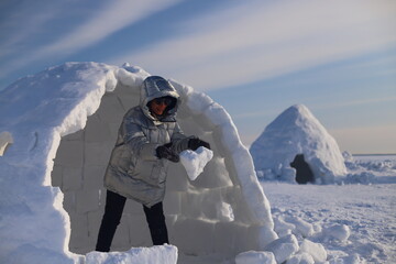 A happy adult woman builds an Igloo out of snow blocks in the Eskimo Village.