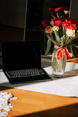 Spring workspace featuring a laptop and a vase of tulips in natural sunlight for online work