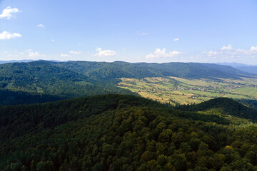 Obraz premium Aerial view of mountain hills covered with dense green lush woods on bright summer day