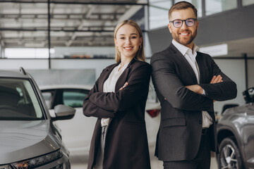 Smiling, friendly car sellers standing in car salon with arms crossed and announcing retail.