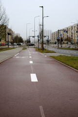 Fototapeta premium Urban street with cycle path and pedestrian walkway surrounded by residential buildings, featuring traffic lights and street signs under a cloudy sky