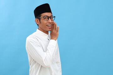 Young asian muslim man puts hand on mouth telling secret rumor, whispering malicious talk conversation