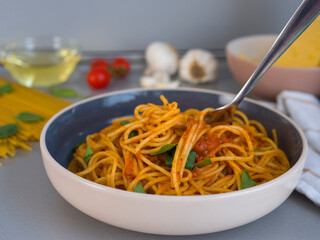 Lifting balanesi pasta twirled with tomato sauce, garnished with fresh basil, resting in contemporary dishware near softly blurred spaghetti and cherry tomatoes