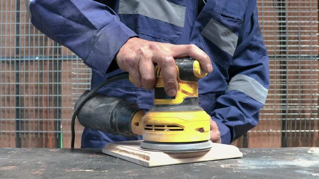 Latin carpenter sanding wood with electric orbital sander, wearing safety glasses in workshop