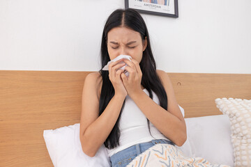 Woman sneezing into tissue while sitting in bed