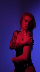 Blonde with a beautiful figure in a black patent leather bodysuit poses in a studio. Studio lighting, low exposure, monochrome red light