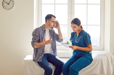 Young man patient talking to female nurse in doctor office in clinic during examination sitting on...
