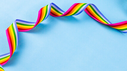 Colorful rainbow ribbon strip on blue pastel background. Concept of cheering LGBT communities all over the world