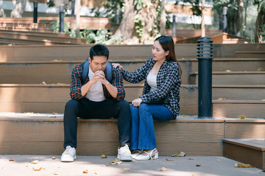 Compassionate female student supporting distressed male peer on campus stairs, offering emotional comfort during academic pressure and personal struggle