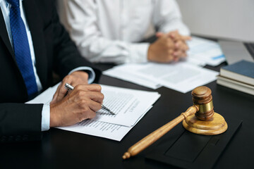 A man is writing on a piece of paper in front of a gavel