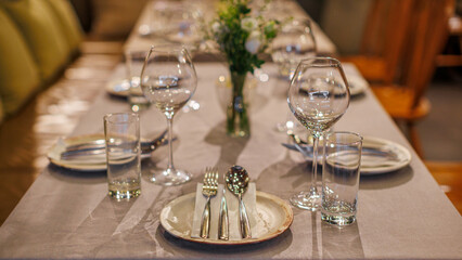 An elegantly set restaurant table with fine dining arrangements, including wine glasses, silverware, and a floral centerpiece, creating a warm and inviting ambiance.