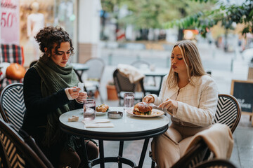 Two friends enjoy a casual meal at an outdoor cafe, seated at a table surrounded by a bustling cityscape in autumn, conveying a sense of companionship and enjoying leisure time together.