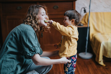 A joyful scene of a mother interacting playfully with her child in a warm, well-lit living room, showcasing the bond of family love and nurturing in an everyday domestic atmosphere.