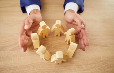 Top view of male entrepreneur employer in suit protecting wooden toy people figures with hands...