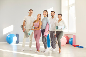 Group of young sporty happy people posing, fitness club sportswomen team holding yoga mats. Active friends before, after exercise or sport instruction, recreational activity together, balance work