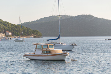 Wooden fishing boat is floating on a calm sea at sunset with sailboats and a forested island in the...