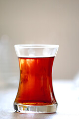 Slim waist tea glass in front of blurry background. Traditional Turkish tea equipment. 