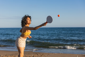 Young woman playing beach tennis on the shore