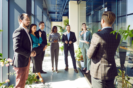 Boss and group of happy business people standing in lobby of modern office. Multicultural team smiling looking at business man. Concept business success, employee appreciation day, common group