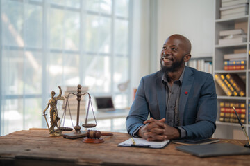 Smiling African American lawyer sitting confidently at his desk in an office, surrounded by justice...