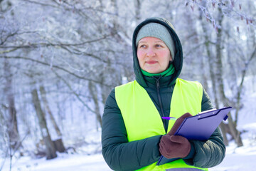 Female ecologist inspects trees in winter. Forestry engineer works in winter. Inspector monitors...