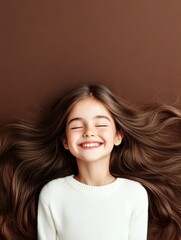 Naklejka premium Joyful Girl with Long Brown Hair - A young girl lies on her back, smiling with eyes closed, showcasing her long, flowing brown hair against a brown background