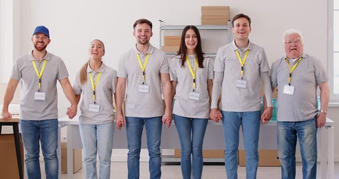 Volunteers in identical clothes and with badges around their necks joyfully raise their hands in air. People of all ages in jeans and t-shirts convey sense of achievement and shared enthusiasm.