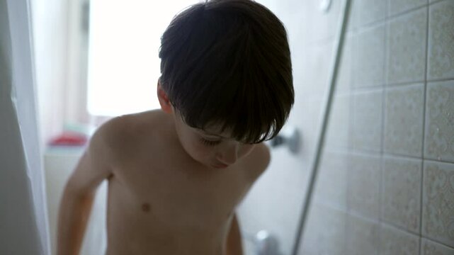 Young boy taking a shower, looking down, with water cascading over his body, capturing a candid and innocent moment of childhood and daily routines